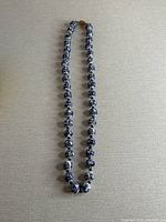 Full view of the necklace laid flat, showing the round porcelain beads painted with blue Chinese motifs over a white background.