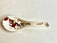 Full view of white porcelain Chinese spoon with hand painted red dragon, green leaves, and red circular detail near handle