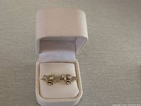 Two bee-shaped earrings displayed in a white cushioned jewelry box, seen from a distance.