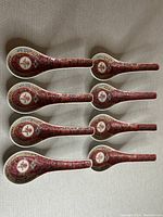 Top view of eight Jingdezhen ceramic spoons arranged in two rows on a beige surface
