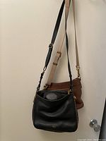 Two leather shoulder bags hanging on a wall hook, one black and one tan brown, showing textures and straps.