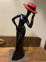 Front view of the Art Deco ceramic figurine depicting a slender woman in a long black dress and red hat on metal stand
