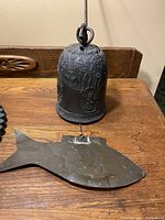 Full side view of antique brass bell with fish wind catcher lying on wooden table