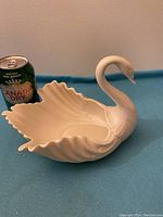 Side view of white Lenox fine china swan figurine showing curved neck and detailed wings, placed next to Canada dry soda can for scale.