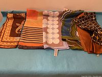 Five mixed patterned luxury scarves laid flat on blue fabric surface showing variety of colors and designs