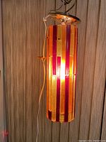 Full view of the cylindrical hanging pendant light with vertical lucite panels in red, yellow, and orange illuminated.