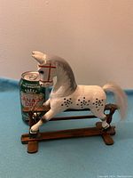 Photo of white wooden rocking horse with black spots, mounted on dark wood rocker base, next to a Canada Dry soda can for scale