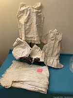Photo of a set of vintage white linen baby clothes including sleeveless top, short-sleeved dress, bloomers, and lace trimmed garments