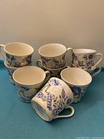 Nine stacked vintage tea cups with blue and green floral and figure designs.