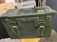 Closed view of vintage military box exterior showing olive drab paint and metal latch clasps on front.