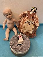 Photo of the three dolls showing the nude bisque baby doll, Bradley Dolls Michelle in patterned dress with tag, and Royal Doulton miniature doll in its box.
