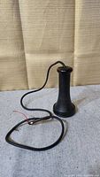 Black antique telephone earpiece standing upright with attached cord lying on surface. Cord has exposed wires at end.