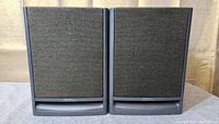 Front view of the pair of Hitachi FX-6 bookshelf speakers showing black cloth grille and vent at bottom with gray surround.