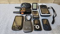 Lot of mixed small electronic devices arranged on fabric surface, including walkie-talkies, GPS units, phones and media players