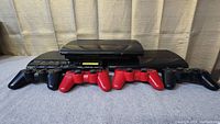 Front view of three Playstation 3 consoles placed side by side with four controllers in front