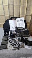 Full kit overview showing Panasonic Mini DV camera model AG-DVC10, multiple batteries, operating instructions, cables, remote control, memory card, and soft camera bag.