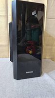 Front view of Samsung PS-FW2-1 passive subwoofer with glossy black surface and Samsung logo at bottom.