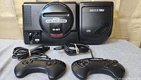Front view of Sega Genesis and Sega CD unit connected, with two wired controllers and two cords placed in front.
