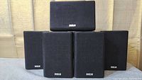 Front view of 5 small RCA speakers stacked; 2 front, 2 rear, 1 center speaker, black with fabric front and RCA logo.
