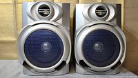 Front view of both Sharp CP-XP300 bookshelf speakers showing the blue mesh woofer grille and oval tweeter casing on each speaker.