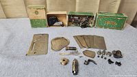 Overview of varied vintage Singer sewing machine parts laid out, including decorative plates, screws, levers, and small mechanisms, some in original packaging boxes