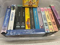 Top-down view of the 14 VHS tapes inside a plastic container showing all spines with titles and editions