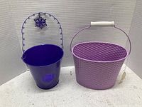 Purple metal bucket with wire handle and snowflake detail beside lavender textured metal basket with white handle