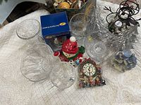 Photo showing various clear glassware items, snowman figure, cookie tin, Christmas clock ornament, snow village figurine, and tree centerpiece.