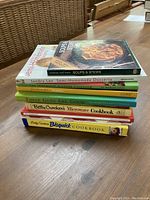 Top-down image of all 10 cookbooks stacked on wooden table showing titles and colorful covers