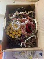 Box of assorted costume jewelry including multiple bracelets and rings of various colors and materials such as plastic beads, metal, woven threads.