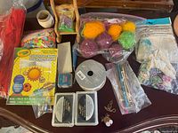 Photo showing variety of crafting items on a table including yarn, ribbons, Crayola Solar System Mobile Kit, fabric pieces, and packaged small accessories.
