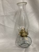 Single clear glass hurricane oil lamp with metal burner assembly.