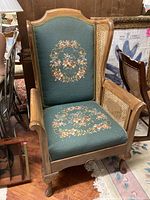 Full view of the large vintage armchair featuring a wooden frame, needlepoint upholstered backrest and seat, and cane sides.