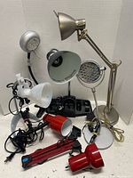 Seven assorted office lamps of various styles, colors, and bases displayed against a white wall.