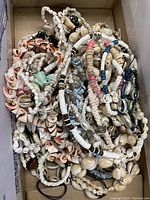Photo of tangled assortment of seashell bracelets and necklaces showing variety of shell types and colors.