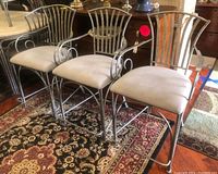 Three metal counter height bar stools with upholstered beige seats on a patterned rug, shown together to illustrate lot contents and design.