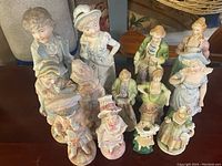 Photo showing front view of thirteen Victorian style porcelain figurines arranged closely together, highlighting details of their faces and clothing.