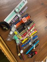 Photo of 25 adjustable wrist watches in various colors and styles spread on wooden floor.