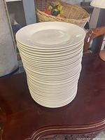 Stack of white ceramic dinner plates stacked on a table, showing the uniform size and shape of the plates.