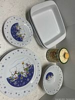 Snowman themed bowls, dinner and salad plates, two white Chantal casserole dishes, and a snowman Earthenware canister captured together.
