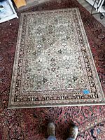 Top-down image showing full view of the 5' x 7' oriental rug placed over a larger dark red patterned rug.
