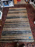 Full view of the rug laid on a larger patterned rug, showing its size and the horizontal striped color pattern.