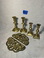 Photo showing all six items; two brass trivets and four brass candlesticks of varying base styles and shapes.