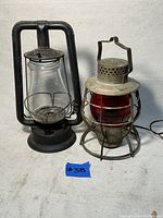 Pair of antique railroad oil lanterns side by side on a white surface, with a blue tag numbered 38