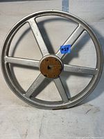 Front view of the large vintage industrial metal wheel or pulley showing 6 spokes and rusted central hub with keyhole