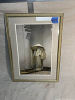 Full view of framed print showing figure in white robe and headdress against gray background.