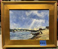 Framed vintage oil painting showing harbor scene with boats near shore and town with church steeple in background, under cloudy sky with sun rays.