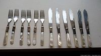 Set of six fish forks and six fish knives laid out on a flat surface, showing mother of pearl handles and silver plated blades.