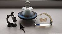 Four items displayed including the frosted glass perfume bottle, butterfly crystal paperweight, and two pewter fairy ornaments, one on a swing and one small figure.