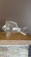 Full side profile view of vintage large clear glass fish-shaped bowl on wooden surface against neutral wall.